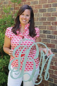Staff photo by Cole Dittmer. Happy Clam Monogram owner and founder Jenny Burnett with one of the company's custom made balsa and birch monogram wall decorations.