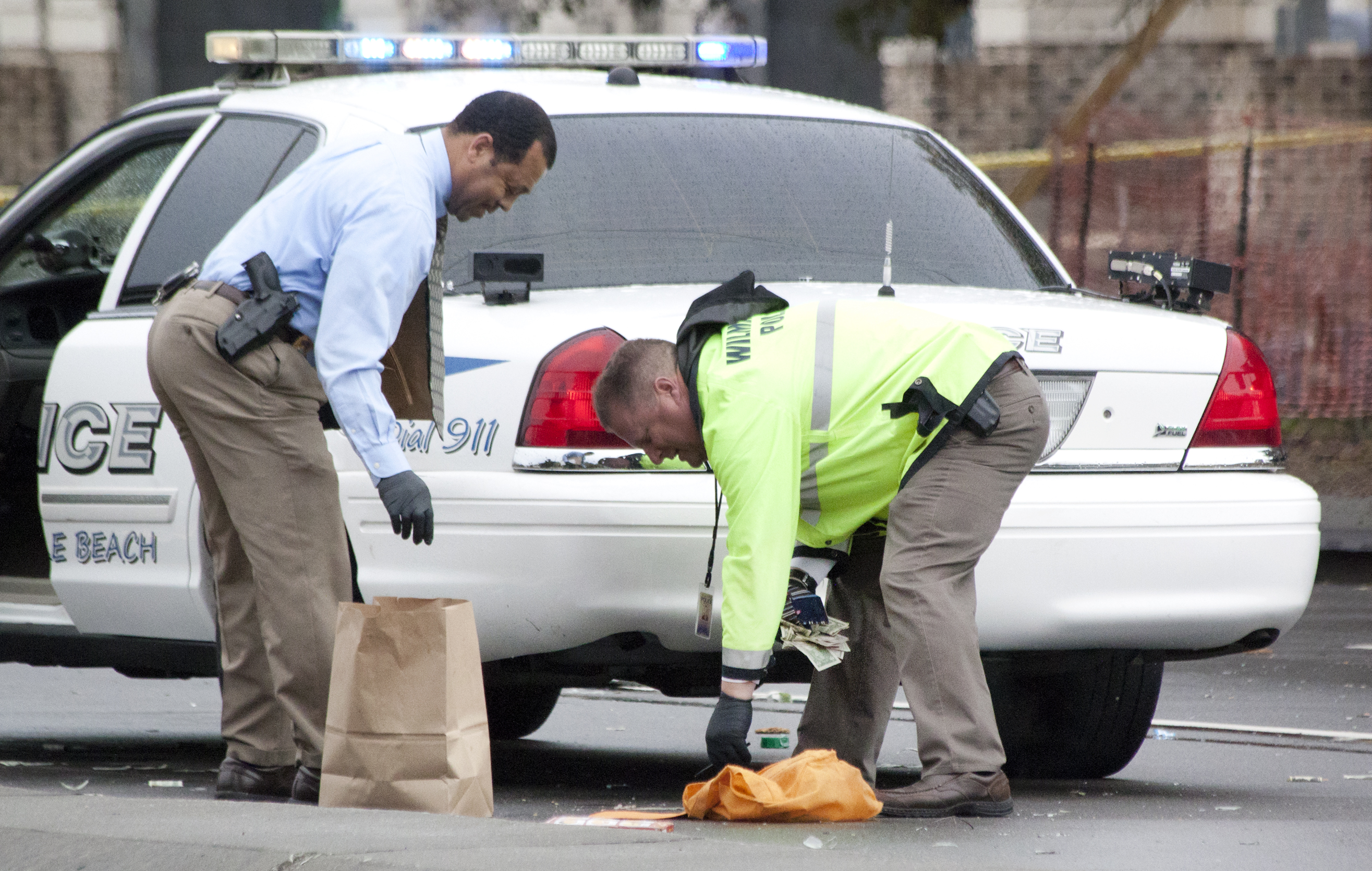 Two officers from the Wilmington Police Department pick up and place in a brown bag money from the bank bag that was strewn along the Wrightsville Avenue roadway after the robbers' car split in two.