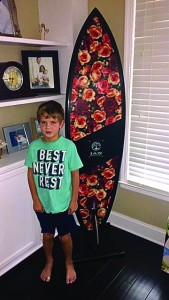 Ryan Carr stands with the 65 Roses surfboard, which his parents bought during Pipeline to a Cure East's live auction. Photo courtesy of Amanda Carr. 